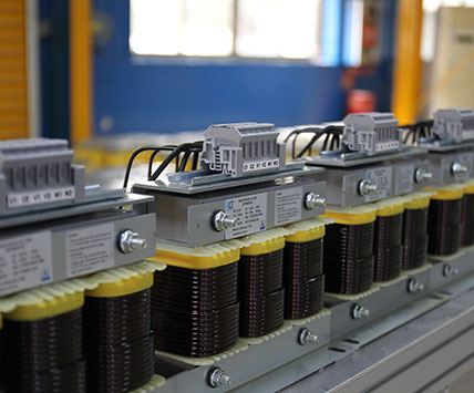 A long batch of three-phase sine wave filters aligned on the factory assembly line for quality inspection.