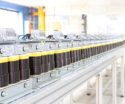 A long batch of three-phase sine wave filters aligned on the factory assembly line for quality inspection.