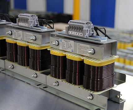 A long batch of three-phase sine wave filters aligned on the factory assembly line for quality inspection.