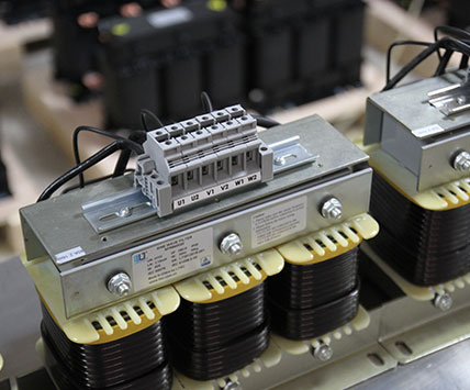 A long batch of three-phase sine wave filters aligned on the factory assembly line for quality inspection.