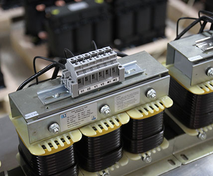 A long batch of three-phase sine wave filters aligned on the factory assembly line for quality inspection.