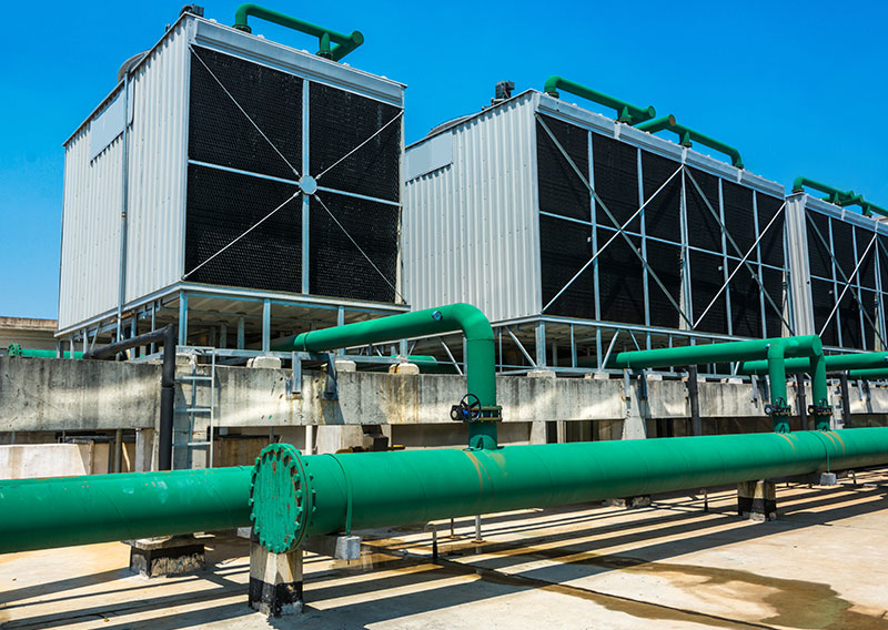 Large commercial HVAC cooling towers and green industrial piping infrastructure, optimized with sine wave filters to erase motor whistling.